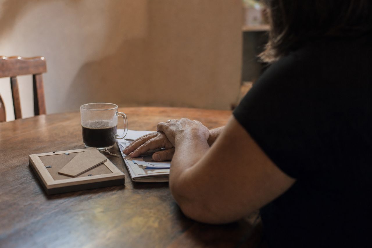 Mesa de casa com porta-retrato virado para baixo, papéis e as mãos de uma mulher