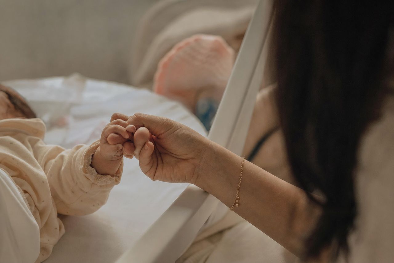 Mão de mulher segurando a mão de um recém-nascido no berço